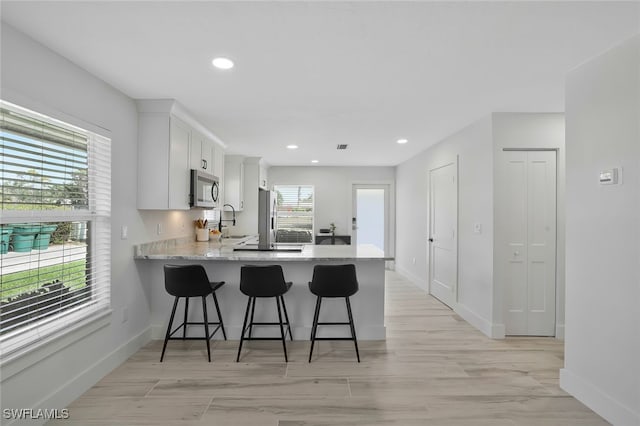 kitchen with a breakfast bar, sink, white cabinets, kitchen peninsula, and light wood-type flooring