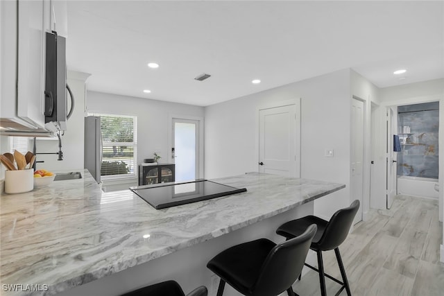 kitchen with white cabinets, a kitchen bar, light hardwood / wood-style floors, kitchen peninsula, and light stone countertops