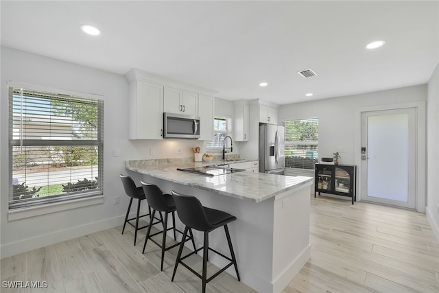 kitchen with a breakfast bar, appliances with stainless steel finishes, light hardwood / wood-style floors, white cabinets, and kitchen peninsula