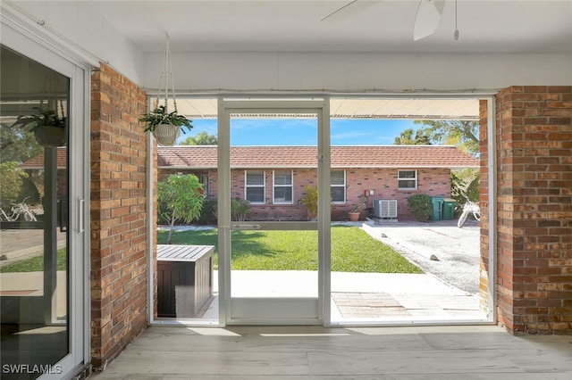 doorway featuring ceiling fan, wood-type flooring, and brick wall