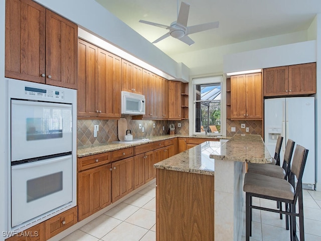 kitchen featuring a kitchen breakfast bar, sink, light tile patterned floors, and white appliances