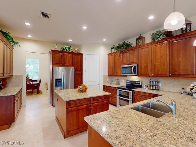 kitchen featuring sink, hanging light fixtures, stainless steel appliances, light stone countertops, and a kitchen island