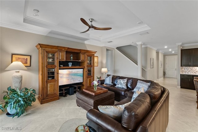 tiled living room featuring a tray ceiling, ceiling fan, crown molding, and decorative columns