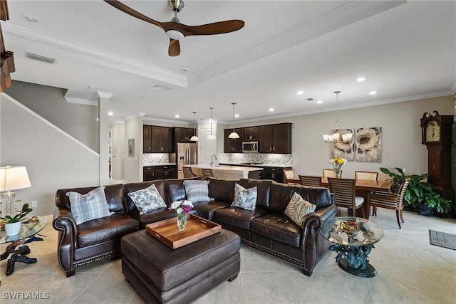 living room featuring ceiling fan with notable chandelier, light tile patterned floors, a raised ceiling, and crown molding