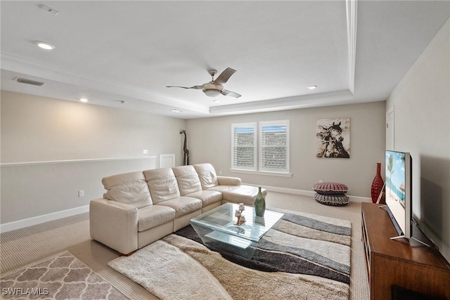 carpeted living room with ceiling fan and a tray ceiling