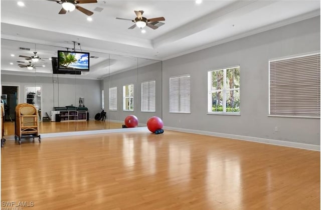 exercise room featuring ornamental molding, light hardwood / wood-style floors, a raised ceiling, and ceiling fan