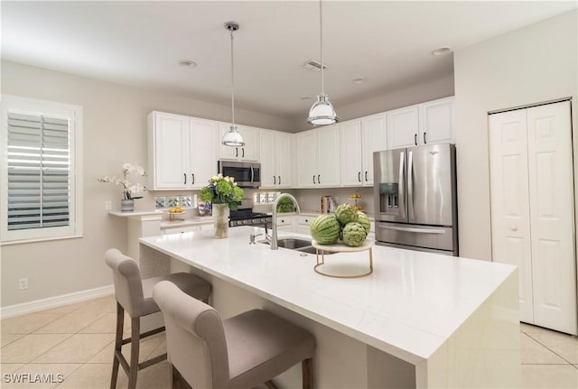 kitchen with appliances with stainless steel finishes, hanging light fixtures, a center island with sink, and white cabinets