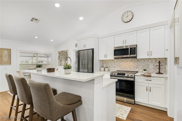 kitchen with white cabinetry, stainless steel appliances, a kitchen breakfast bar, and a center island with sink