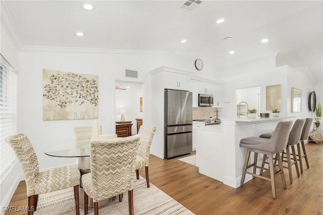 kitchen featuring a breakfast bar, wood-type flooring, appliances with stainless steel finishes, kitchen peninsula, and white cabinets