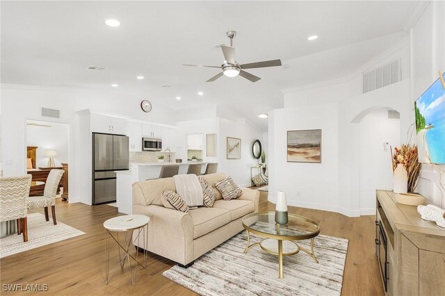 living room with lofted ceiling, crown molding, light hardwood / wood-style floors, and ceiling fan