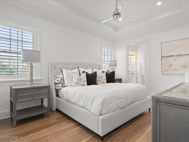 bedroom featuring connected bathroom, hardwood / wood-style flooring, ornamental molding, and a raised ceiling