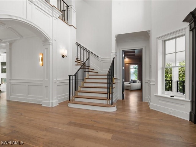 foyer entrance with ornate columns, wood-type flooring, and a towering ceiling