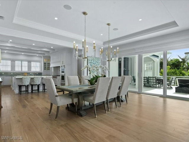 dining area featuring light hardwood / wood-style flooring, ornamental molding, a raised ceiling, and a healthy amount of sunlight