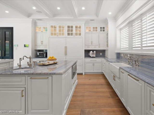 kitchen with white cabinetry, sink, stainless steel microwave, and light stone counters