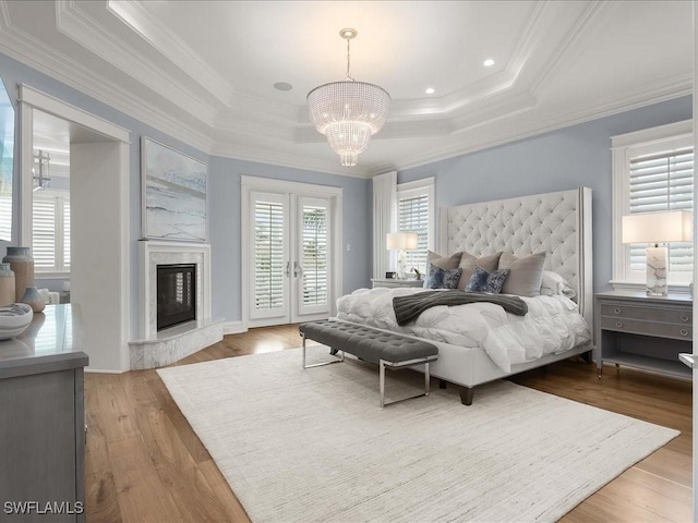 bedroom with wood-type flooring, access to outside, ornamental molding, a raised ceiling, and a premium fireplace