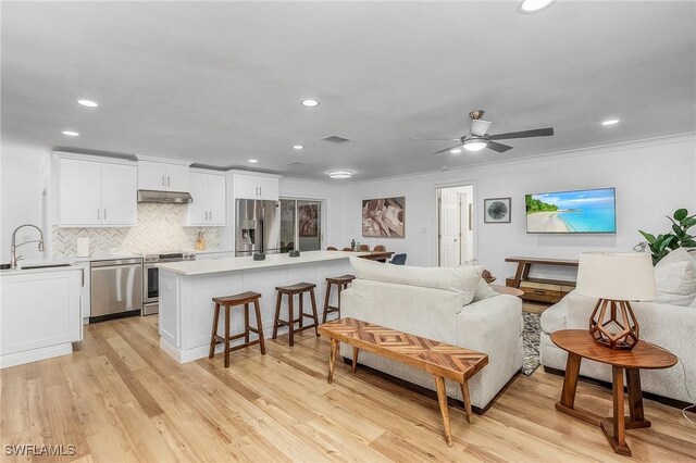 living room featuring crown molding, ceiling fan, sink, and light wood-type flooring