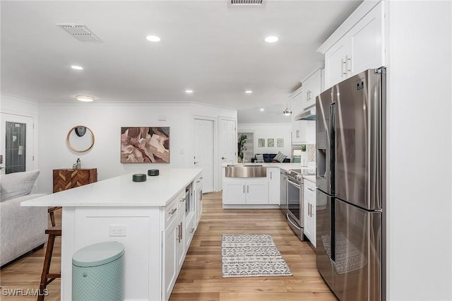 kitchen featuring stainless steel appliances, light hardwood / wood-style floors, white cabinets, a kitchen bar, and kitchen peninsula