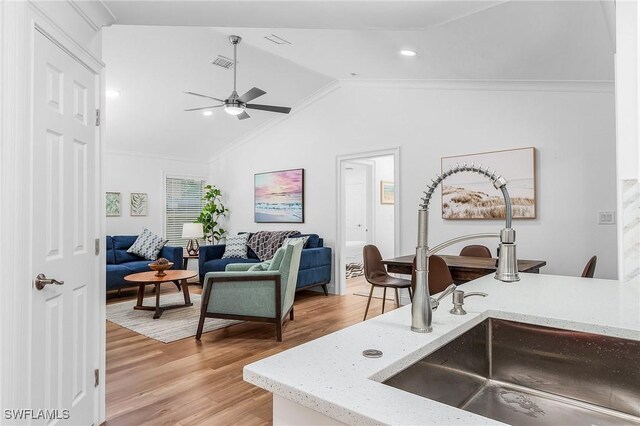 kitchen featuring lofted ceiling, sink, light wood-type flooring, ceiling fan, and light stone countertops