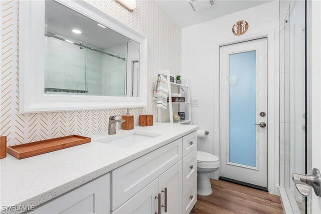 bathroom with toilet, vanity, a shower with door, hardwood / wood-style flooring, and backsplash