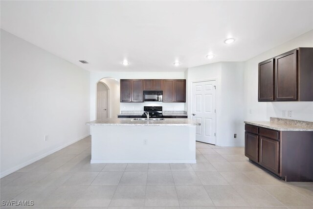 kitchen with dark brown cabinetry, sink, light stone counters, an island with sink, and electric stove