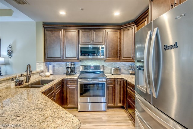 kitchen featuring tasteful backsplash, sink, light stone countertops, and appliances with stainless steel finishes