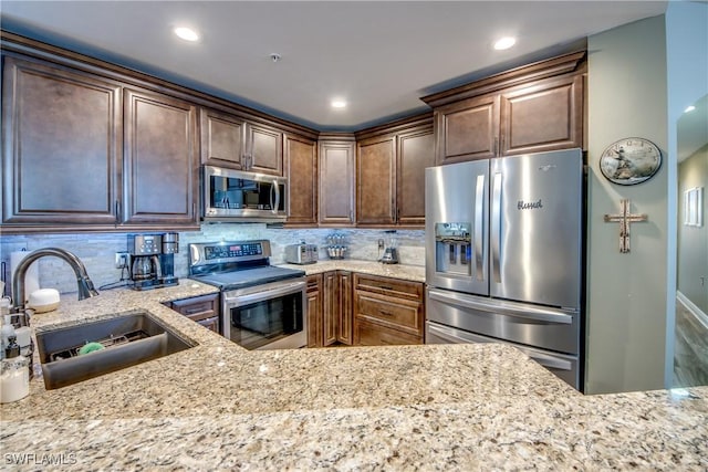 kitchen featuring tasteful backsplash, sink, light stone counters, and stainless steel appliances