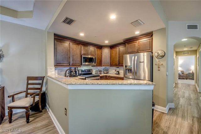 kitchen featuring backsplash, stainless steel appliances, kitchen peninsula, and light wood-type flooring