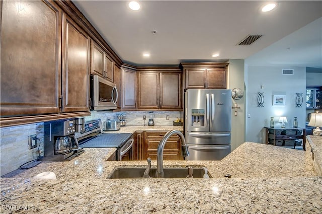 kitchen with tasteful backsplash, appliances with stainless steel finishes, sink, and light stone counters