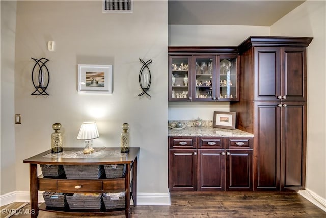 bar with light stone countertops, dark wood-type flooring, and dark brown cabinets