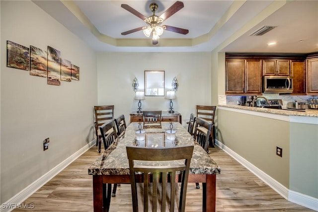 dining space featuring wood-type flooring, ceiling fan, and a tray ceiling