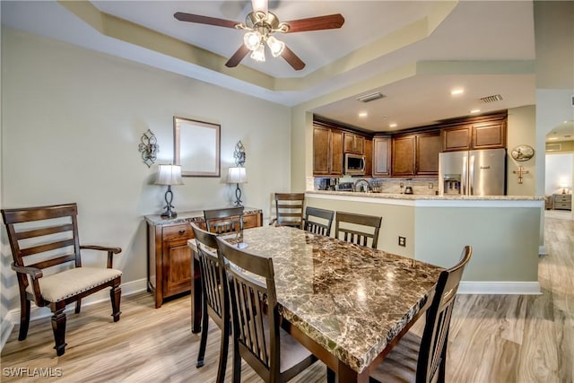 dining area with a raised ceiling, ceiling fan, and light wood-type flooring