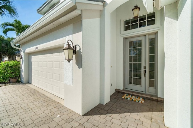 view of exterior entry with stucco siding, driveway, and a garage