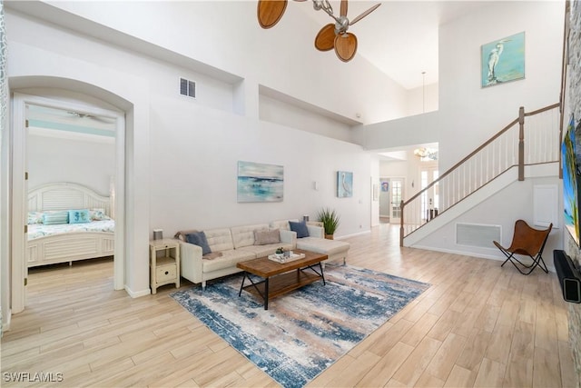living area featuring light wood finished floors, a ceiling fan, visible vents, and stairs