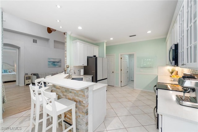 kitchen with a sink, stainless steel microwave, visible vents, freestanding refrigerator, and decorative backsplash