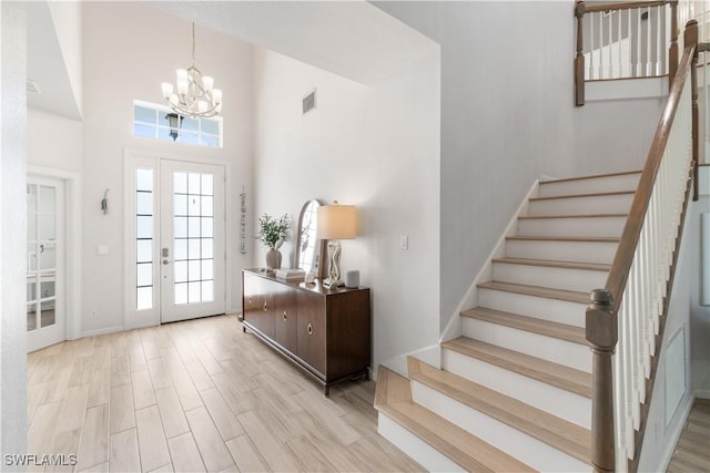 entrance foyer with stairway, a high ceiling, an inviting chandelier, wood finished floors, and visible vents