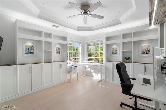 office area featuring a tray ceiling, a ceiling fan, crown molding, light wood-style flooring, and built in shelves