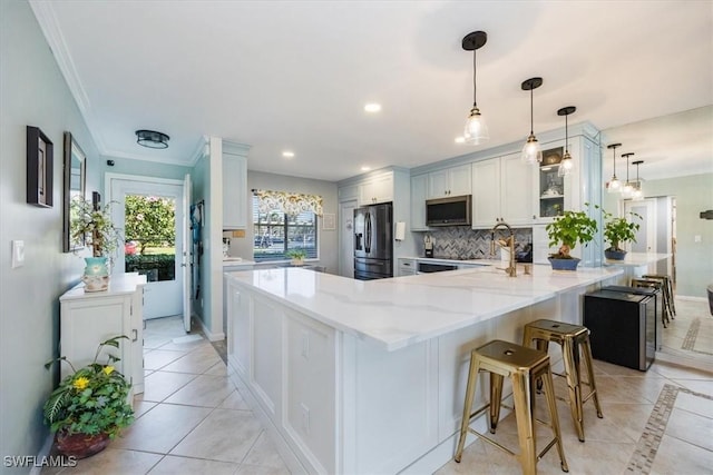 kitchen featuring light stone counters, stainless steel appliances, backsplash, white cabinets, and a peninsula