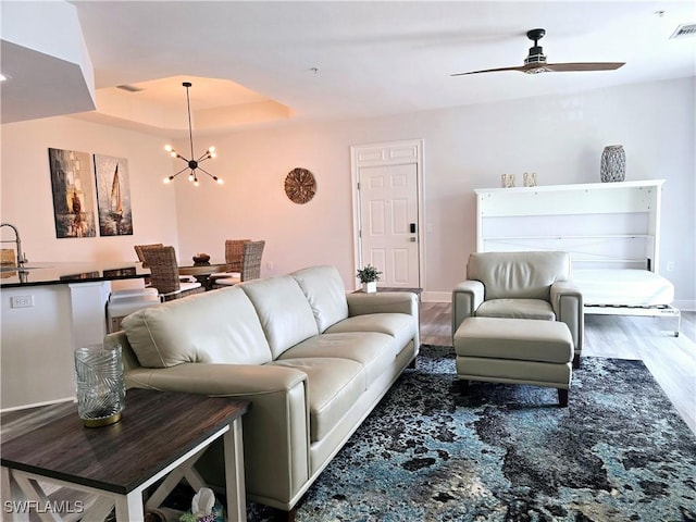 living room featuring sink, dark hardwood / wood-style floors, ceiling fan with notable chandelier, and a tray ceiling