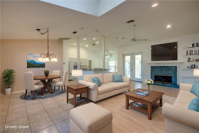 living room featuring high vaulted ceiling, ceiling fan with notable chandelier, and a tile fireplace