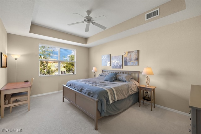 carpeted bedroom featuring a tray ceiling and ceiling fan