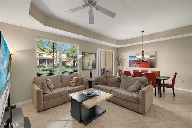 tiled living room with a tray ceiling and ceiling fan with notable chandelier