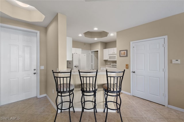 kitchen featuring white cabinetry, white appliances, a kitchen bar, and kitchen peninsula