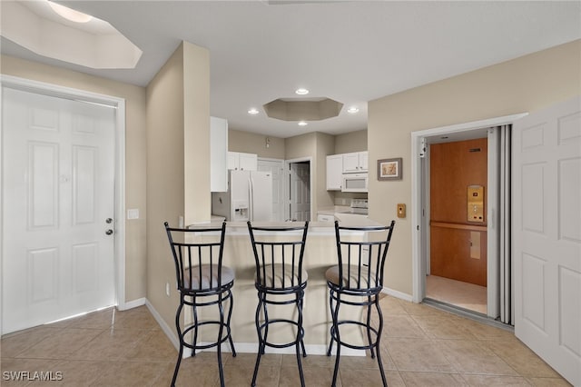 kitchen featuring a breakfast bar, white cabinetry, light tile patterned floors, kitchen peninsula, and white appliances