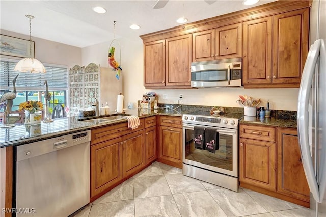 kitchen featuring brown cabinets, stainless steel appliances, hanging light fixtures, a sink, and dark stone countertops