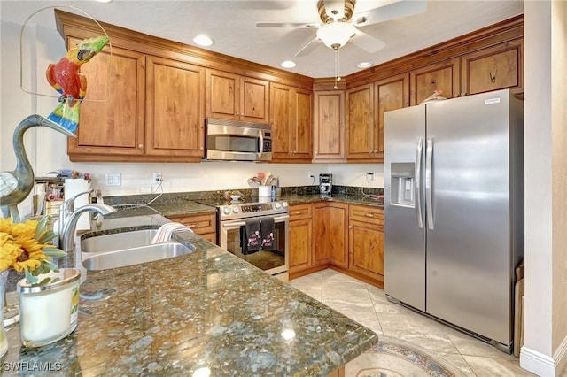 kitchen featuring dark stone countertops, appliances with stainless steel finishes, brown cabinetry, and a sink