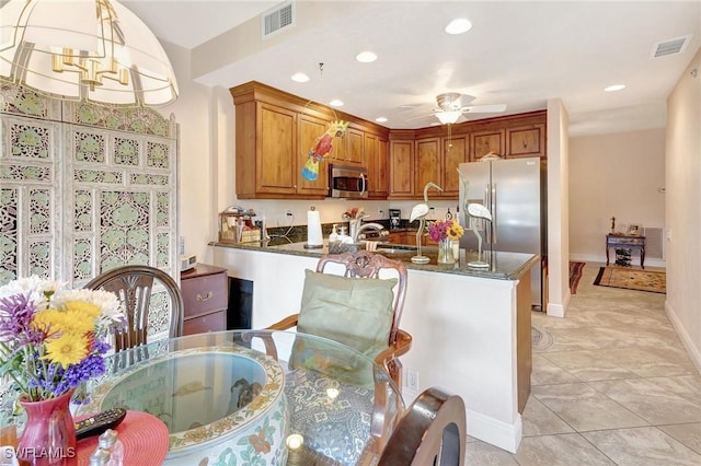 kitchen featuring visible vents, appliances with stainless steel finishes, brown cabinetry, and decorative light fixtures