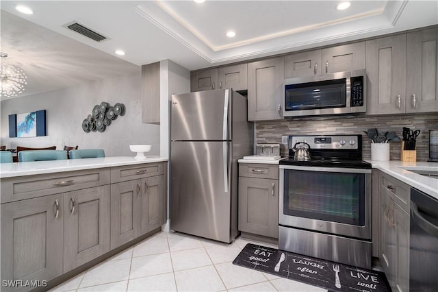 kitchen with light tile patterned flooring, tasteful backsplash, appliances with stainless steel finishes, a tray ceiling, and gray cabinets