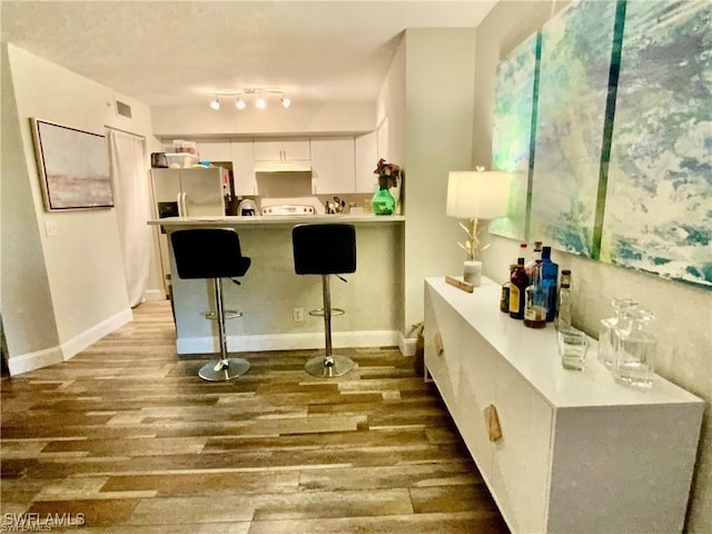 kitchen featuring a breakfast bar, stainless steel fridge with ice dispenser, white cabinetry, hardwood / wood-style flooring, and kitchen peninsula