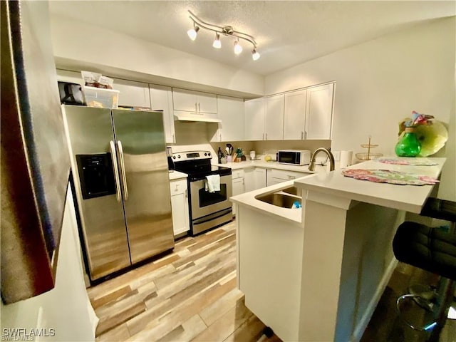 kitchen featuring white cabinetry, appliances with stainless steel finishes, a kitchen bar, and kitchen peninsula