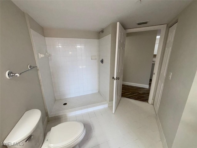 full bath with baseboards, a tile shower, visible vents, and toilet